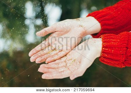 Young curly girl in crystal sunglasses blowing on hands with golden glitters on blue background.