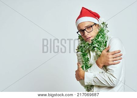 a man with a green tinsel on his neck holds himself by the shoulders, a light background, free space for copying, a new year.