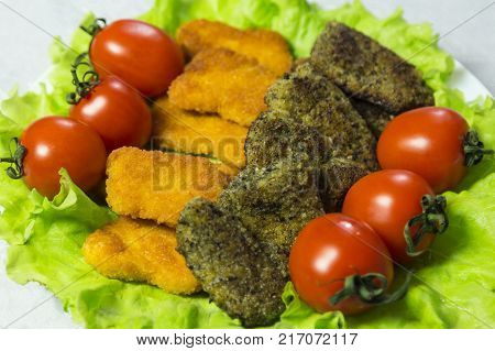 Close-up. Chicken nagets in a plate on green lettuce leaves decorated with tomatoes.