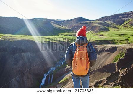 back view of woman traveler with small orange backpack on a walk in the Valley of the river of Hveragerdi Iceland. Hiking Tour of Reykjadalur Hot Springs