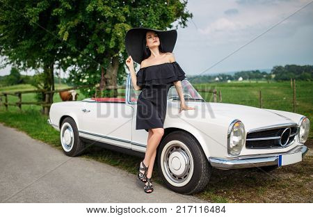 Beautiful young girl in a black hat driving vinage car