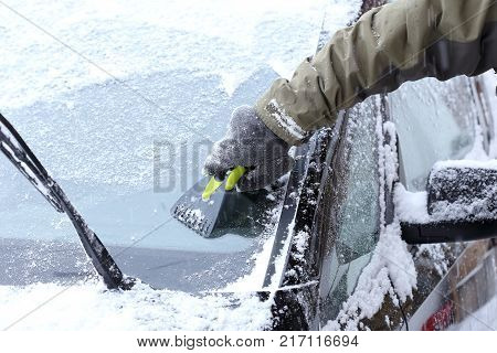 hand is scraping a wind screen of a car
