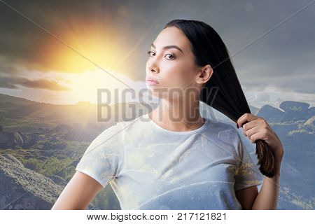 New shampoo. Pretty serious young woman standing and touching her hair after using new expensive shampoo and feeling satisfied with it