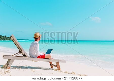 young man working on laptop at tropical beach, remote work concept