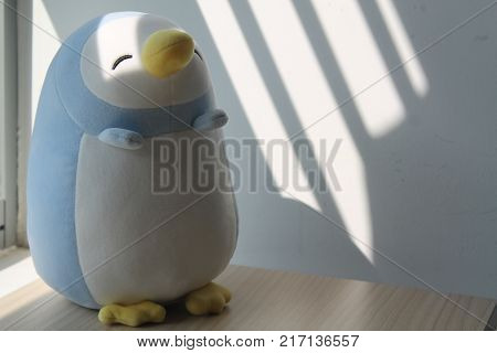 Blue penguin toy sitting by the window in shadows