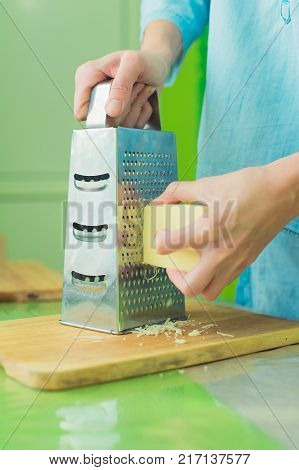 Close-up of a woman's hands rub a parmesan cheese on a metal grater on a green table