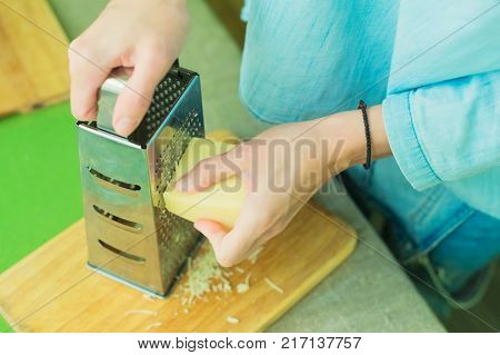 Close-up of a woman's hands rub a parmesan cheese on a metal grater on a green table