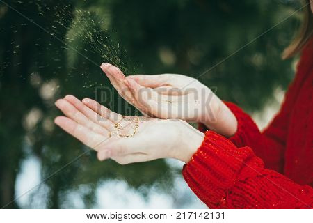 Young curly girl in crystal sunglasses blowing on hands with golden glitters on blue background.