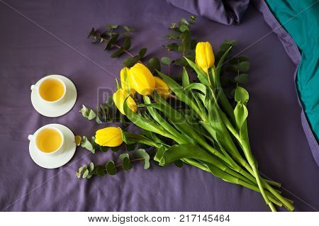 Yellow tulips and two cups of tea in bed, morning