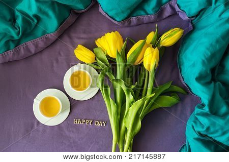 Yellow tulips and two cups of tea in bed, close-up, lettering happy day