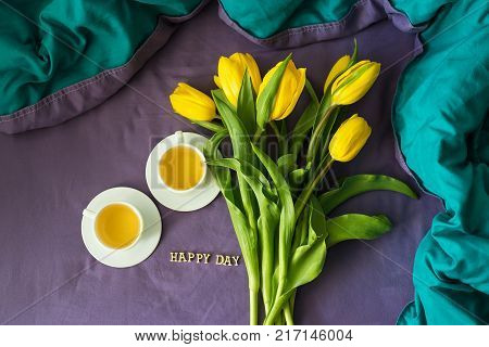 Yellow tulips and two cups of tea in bed, close-up, lettering happy day