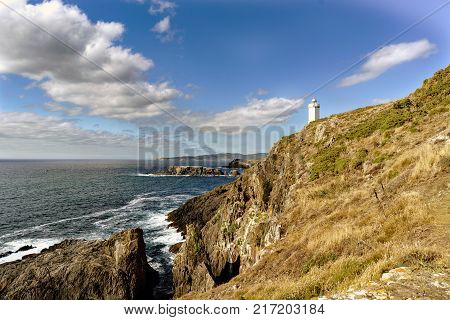 View of Mera lighthouse on a cliff on the atlantic coast of Spain in La Coruña. Sky with clouds and sun facing