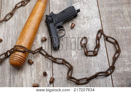 A rusty chain with a bat, a gun, bullets scattered lies on a wooden background. View from above