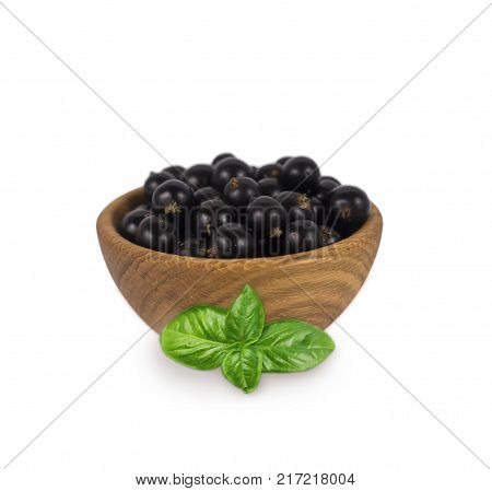 Blackcurrant with basil in a wooden bowl with copy space for text. Ripe and tasty black berry isolated on white. Currant on a white background.