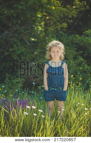 Cute Blond Young Girl Child Stylish Dressed In Blue Jeans Dress Posing On Meadow Of Forest Wild Mayw
