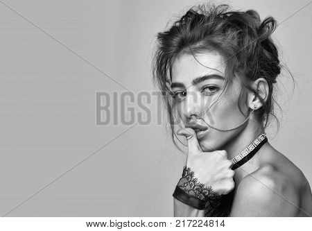Pretty girl or beautiful woman young cute sexy fashion model with curly hair nose ring and necklace with cuffs poses with thumb on lips on grey background copy space