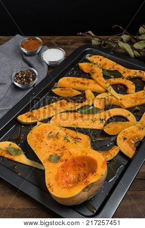 Preparation of butternut pumpkin sliced with salt sweet pepper pepper and thyme in baking dish. Cooking process