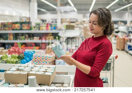 Smart modern female housewife customer choosing cup or mug in a big supermarket malla