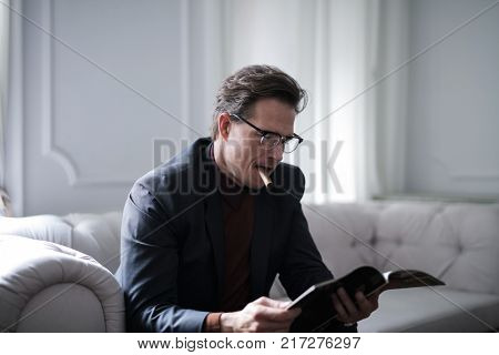 Handsome businessman smoking a cigar while reading a magazine
