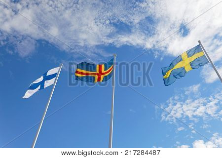 Flags from Finland Aland and Sweden on flag poles blue sky and white cloudes