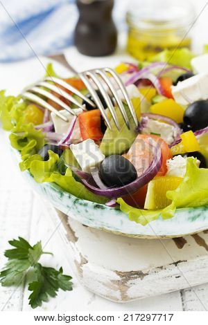 Greek salad in a ceramic plate on a white wooden background. Traditional Greek dish. Selective focus.Top view.