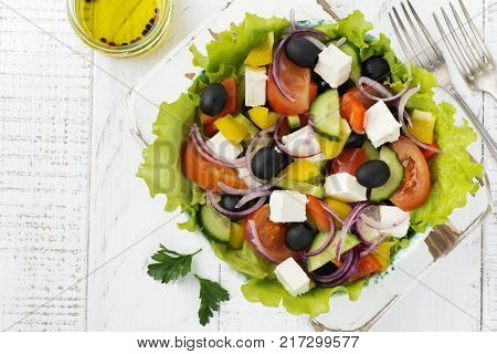 Greek salad in a ceramic plate on a white wooden background. Traditional Greek dish. Selective focus.Top view.