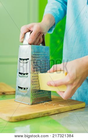 Close-up of a woman's hands rub a parmesan cheese on a metal grater on a green table