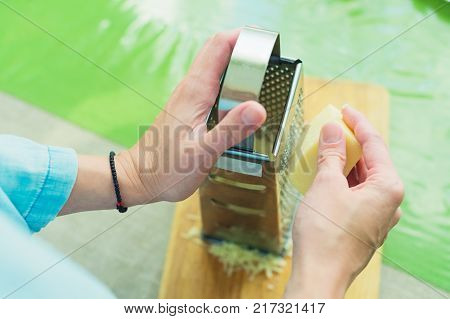 Close-up of a woman's hands rub a parmesan cheese on a metal grater on a green table