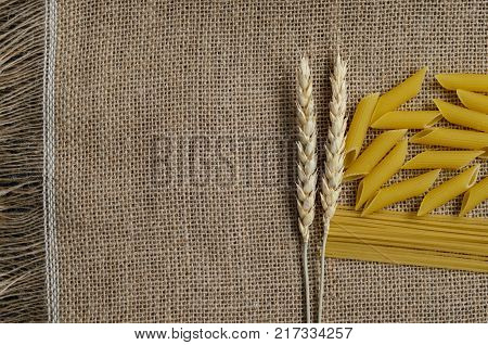 Still life for a kitchen of wheat ears and pasta from wheat on a sackcloth background.