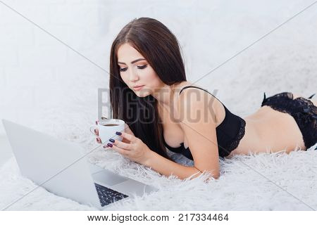 Pretty sexy young woman laying on the bed with couple of coffee in a black lace underwear on the white background. Close up of lady. Beauty concept.