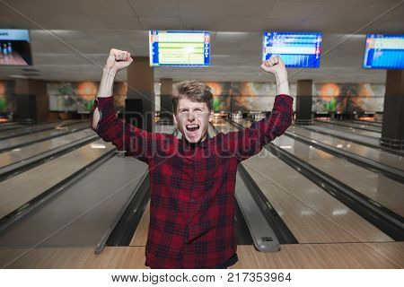 Happy young man made a bowling strike. The student raised his hands from joy while playing bowling. Bowling victory