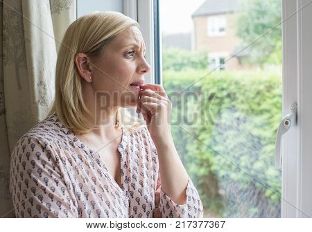 Sad Woman Suffering From Agoraphobia Looking Out Of Window