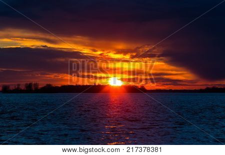 A Winter Sunset on the Lakeshore in Lachine Quebec. The silhouette of a  leafless tree, against  the blue sky and orange clouds on a cold winters afternoon, illuminate the scene.