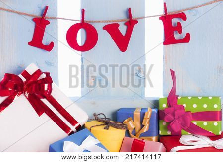 Love word and colorful presents - Love written from red paper letters and tied to a string with wooden clips on a blue wooden fence and an abundance of multicolor gift boxes.