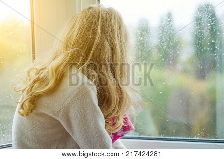 A child in pajamas smiles in an autumn window with rain drops. Back view.