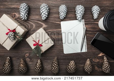 Brown wood background. Gold cones and sweet biscuits arranged diametrically opposed. Gifts, letter, phone, star and coffee, space for a greeting message. Top View.