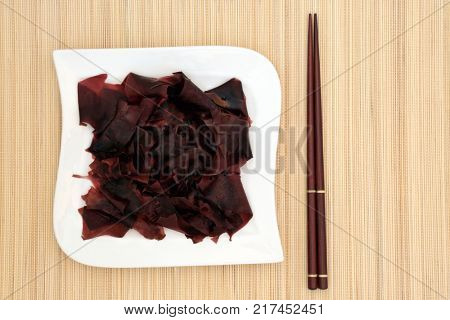 Dulse seaweed health food on a porcelain square shaped dish and chopsticks on bamboo background. Superfood very high in minerals and has many health benefits..