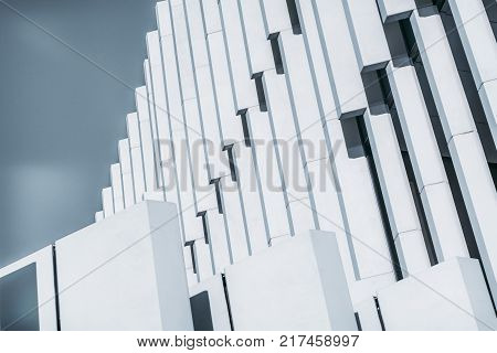 Side view of abstract white contemporary building facade with thick concrete vertical striped blocks; close-up view of outdoor bright exterior of modern house with sky in background
