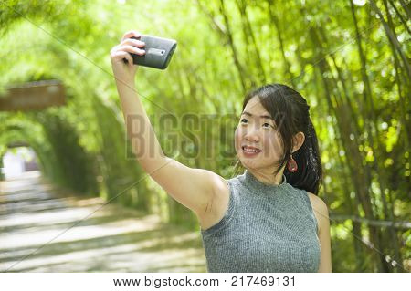 young pretty Chinese Asian woman enjoying having fun taking selfie picture with mobile phone camera posing cool at beautiful nature background in tourist travel and holiday photo concept