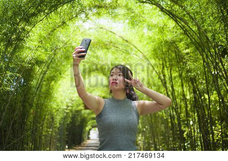 young pretty Chinese Asian woman enjoying having fun taking selfie picture with mobile phone camera posing cool at beautiful nature background in tourist travel and holiday photo concept