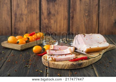 A smoked ham sliced with a knife and yellow cherry tomatoes on a wooden rustic cutting board
