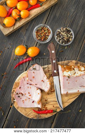A sliced smoked meat with spice and tomatoes on a dark wooden rustic background top view