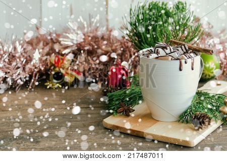 Hot chocolate in white cup topping with marshmallow and chocolate sauce. Homemade hot chocolate or cacoa on wood table with copy space in Christmas theme and snowfall background. Concept of Christmas drink. Delicious hot chocolate for Christmas party.