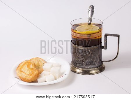 Glass with tea and teaspoon in old silver glass-holder sugar pieces and cakes on white background