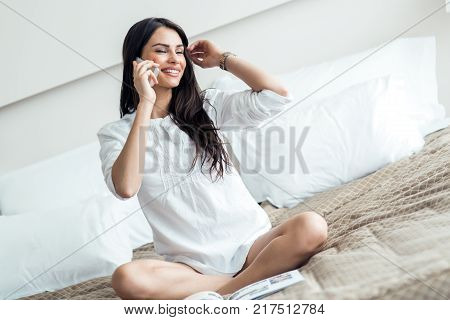 Beautiful woman in a shirt talking on the phone and reading the morning paper on the luxorious bedroom bed
