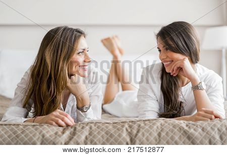 Two beautiful girls talking and smiling while lying on a luxorious  bed