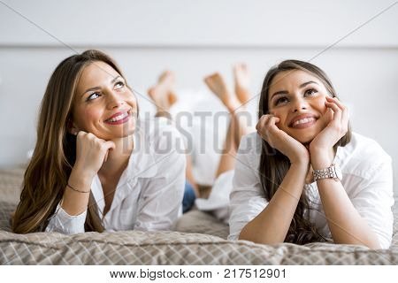 Two beautiful girls talking and smiling while lying on a luxorious  bed