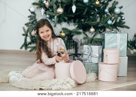 The girl sits at the tree and looks at the gifts. New Year holidays. The time to realize dreams. A gift in the box. New Year's Symbol