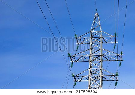 The support of the overhead power line is 35 kilovolts. Electricity. The support is silvery. Insulators are green. The wires diverge in different directions. Blue sky background.