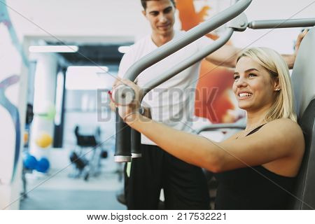 Beautiful woman exercising in gym with some help by personal trainer